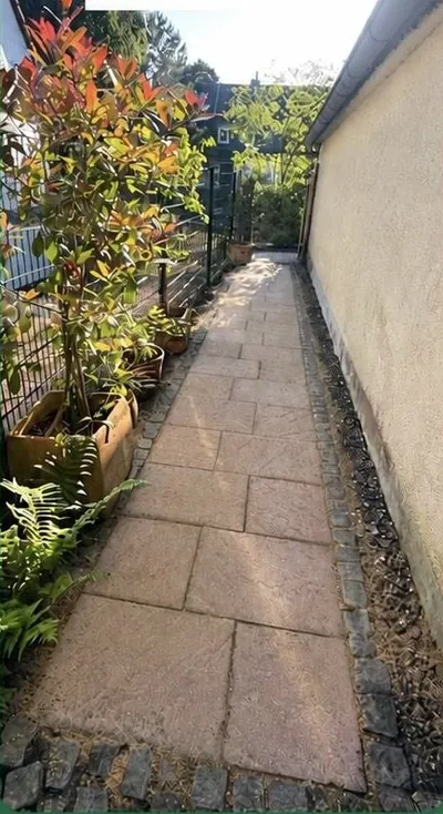 Derselbe Gartenweg nach der Reinigung: sauberer Plattenbelag, freigeräumte Ränder, Bepflanzung.