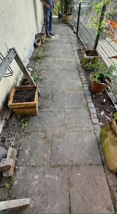 Schmaler Gartenweg vor der Reinigung: verschmutzte Platten, am Rand abgestelltes Gerümpel.