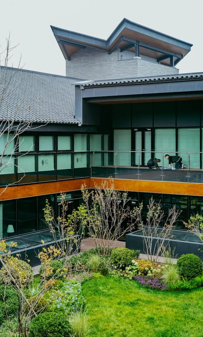 Zweigeschossiges Objekt mit umlaufender Glasfront und begrüntem Innenhof, im Obergeschoss reinigt eine Person die Fensterfront.