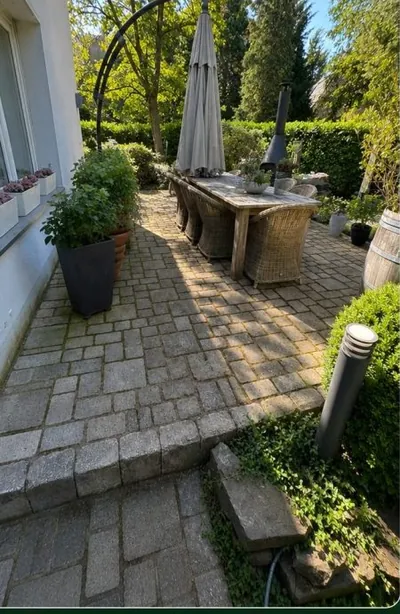 Terrasse mit Natursteinpflaster vor der Reinigung: graue, algenbelegte Steine im Schatten.